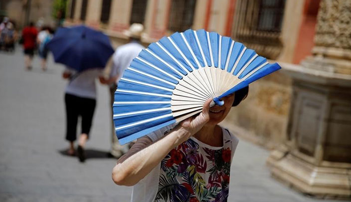 امرأة تستخدم مروحة يدوية لتحمي وجهها من الشمس في إشبيلية بإسبانيا