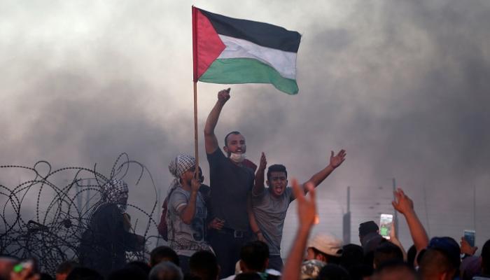 شبان فلسطينيون يحملون العلم قرب السياج الحدوي - رويترز