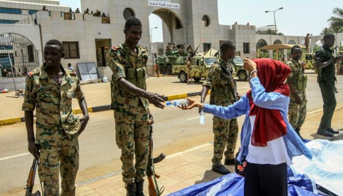 سودانية تقدم قارورة ماء لعسكري أثناء تجمع أمام مقر قيادة الجيش بالخرطوم