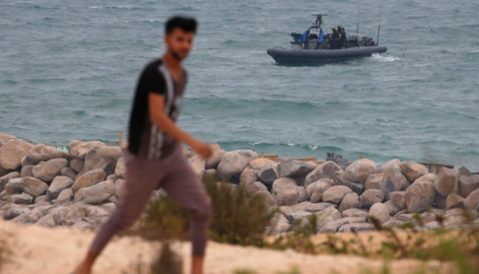فلسطيني يمشي على سواحل غزة ويظهر في الصورة قارب إسرائيلي