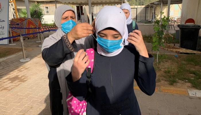 معلمة تساعد إحدى الطالبات في ارتداء الكمامة