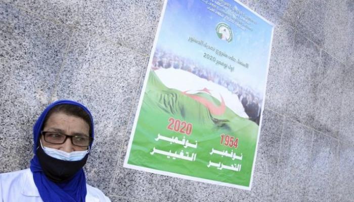 سيدة جزائرية أمام ملصقة انتخابية خاصة باستفتاء تعديل الدستور
