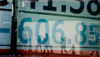 أحد المشاة يرتدي قناعا للوجه يمر عبر لوحة تعرض مؤشر نيكي 225 