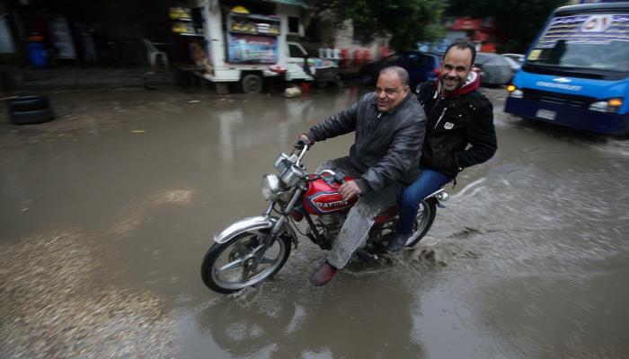 مصريان يركبان دراجة نارية خلال عاصفة رعدية وأمطار غزيرة في وسط القاهرة