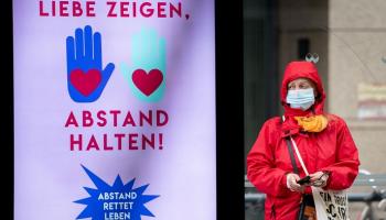 ألمانية ترتدي الكمامة بجوار إعلان "أظهر حبك.. وابق بعيدا"