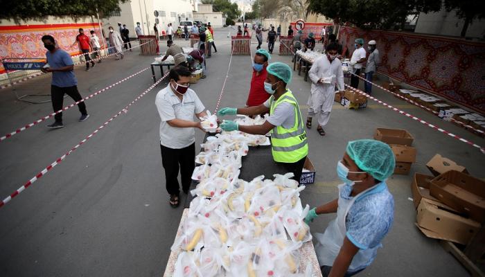 متطوعون يرتدون أقنعة وقفازات واقية يوزعون وجبات الإفطار في المنامة