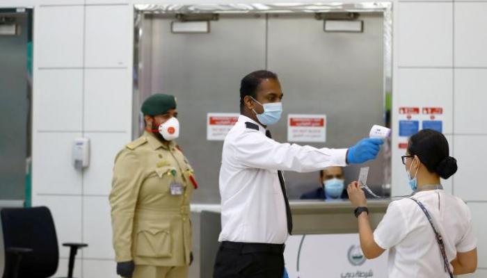 رجل أمن يقيس درجة حرارة سيدة قبل السماح بدخولها منشأة في دبي