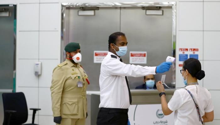 رجل أمن يقيس درجة حرارة سيدة قبل السماح بدخولها منشأة في دبي