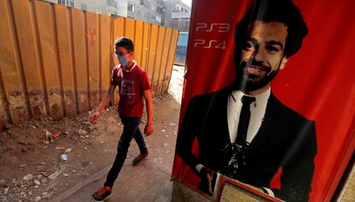 شاب مصري يرتدي الكمامة يمر بجوار ملصق لصورة اللاعب المصري محمد صلاح