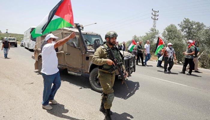 متظاهرون يحملون أعلامًا فلسطينية بينما يقف جندي إسرائيلي -رويترز