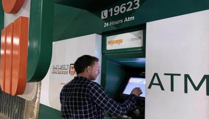 شاب يقوم بعملية سحب أموال من ماكينة صراف آلي تابعة للبنك الأهلي المصري