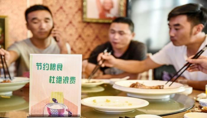 صينيون يتناولون الطعام وبجوارهم لافتة تدعو إلى عدم إهدار الغذاء 