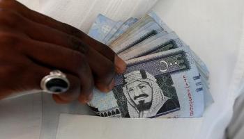مواطن سعودي يعرض عملات ورقية بالريال السعودي في متجر للصرافة بالرياض