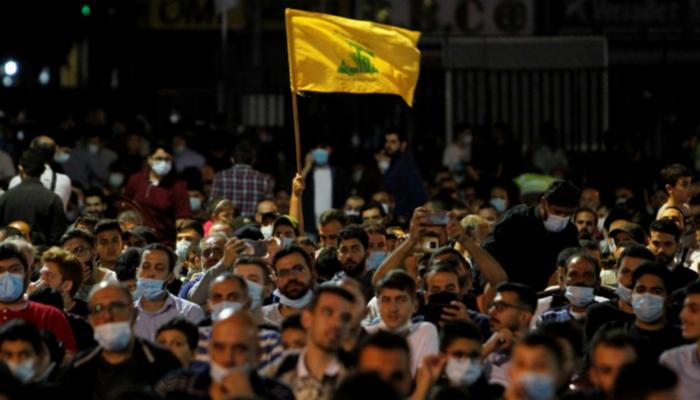 راية حزب الله يرفعها مشارك بأحد مؤتمرات المليشيات الموالية لإيران