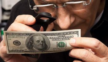 صراف يتحقق من ورقة بمائة دولار - أرشيف