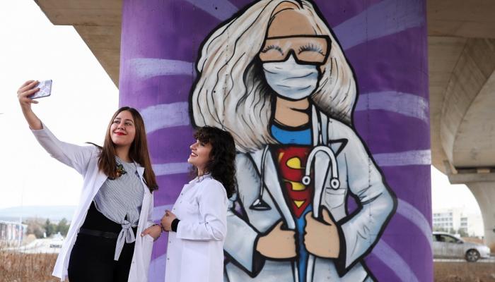 طالبتان بكلية طب تركية تلتقطان سيلفي أمام جرافيتي عن جائحة كورونا
