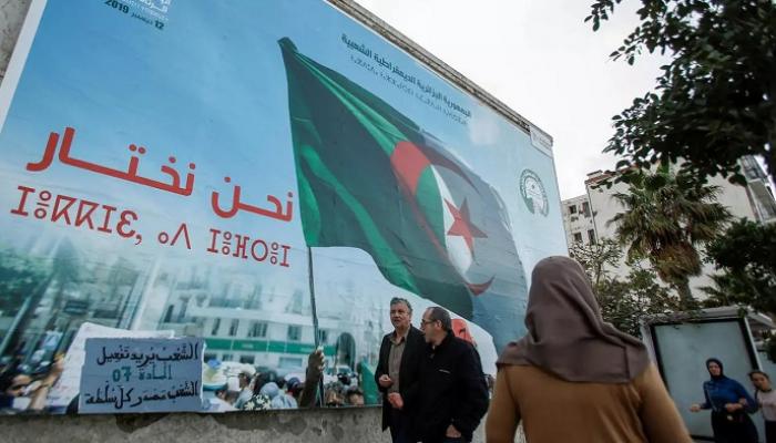 جزائريون يسيرون بجانب ملصق انتخابي