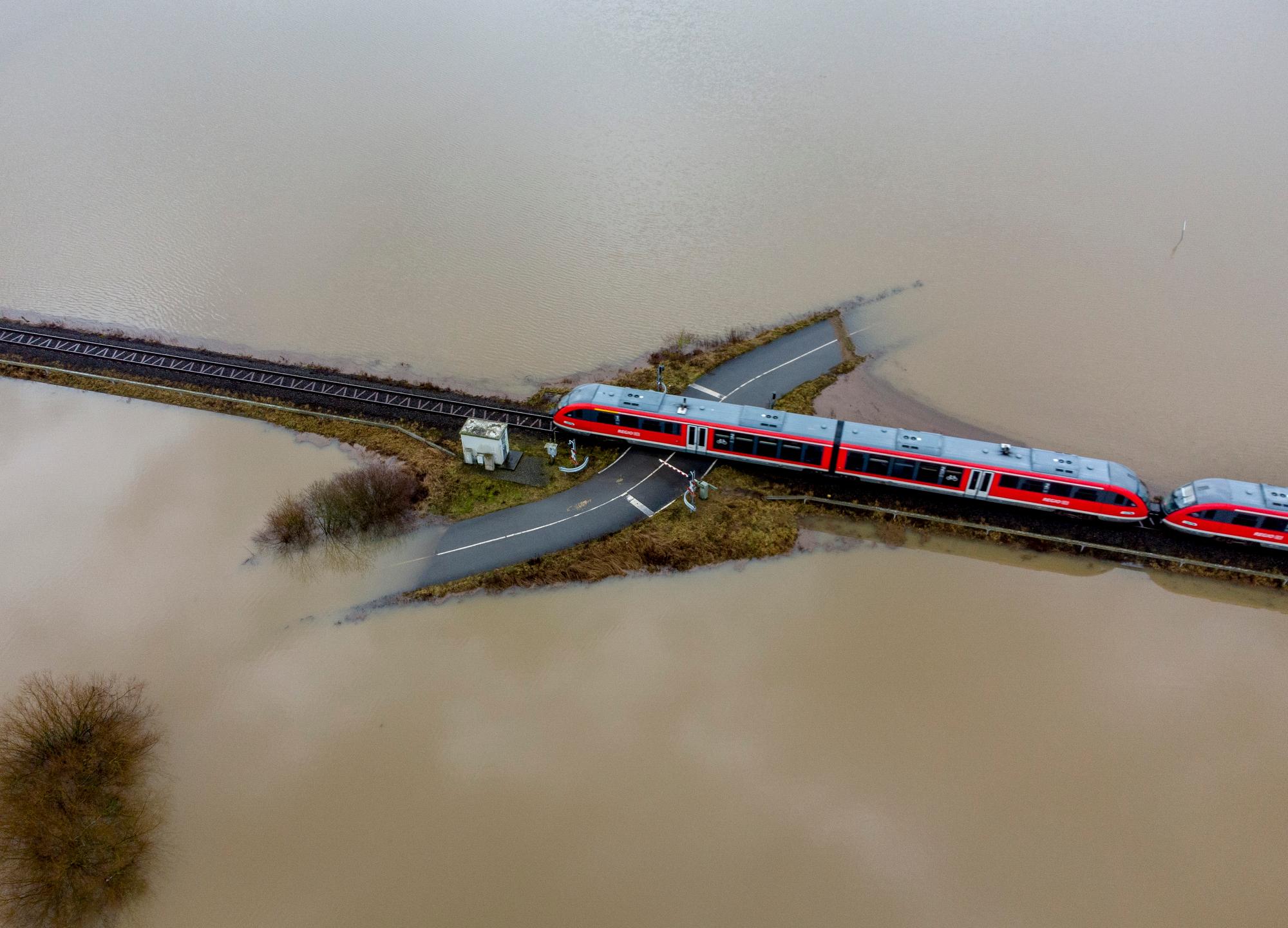 قطار از یک گذرگاه راه‌آهن عبور می‌کند که توسط آب‌های سیلاب ناشی از باران و ذوب برف در نزدیک فرانکفورت، آلمان احاطه شده است