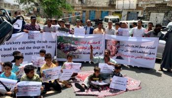 يمني ومجموعة من الأطفال يفترشون الأرض خلال وقفة احتجاجية بتعز 