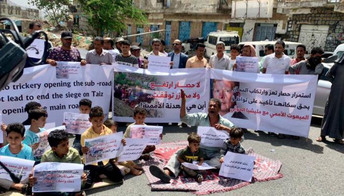 يمني ومجموعة من الأطفال يفترشون الأرض خلال وقفة احتجاجية بتعز