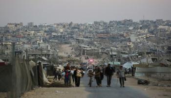 فلسطينيون يسيرون على طول الطريق أمام المباني المدمرة في خان يونس