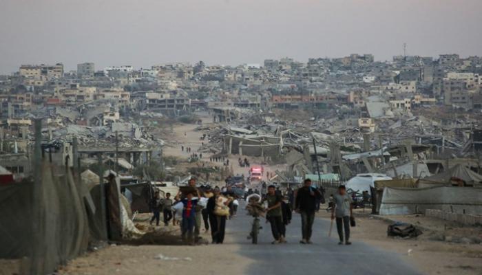فلسطينيون يسيرون على طول الطريق أمام المباني المدمرة في خان يونس