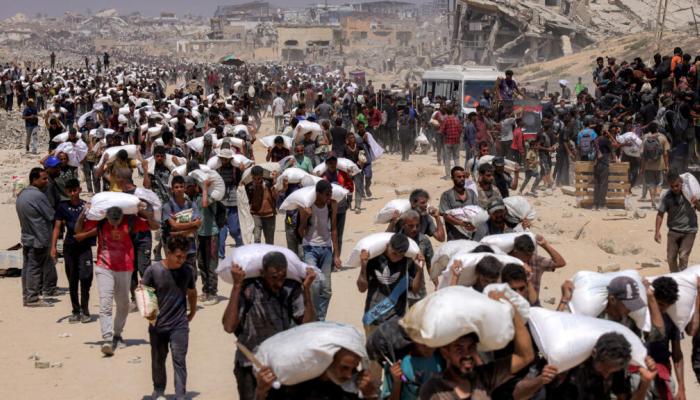 فلسطينيون في غزة يحملون أجولة المساعدات - أرشيفية