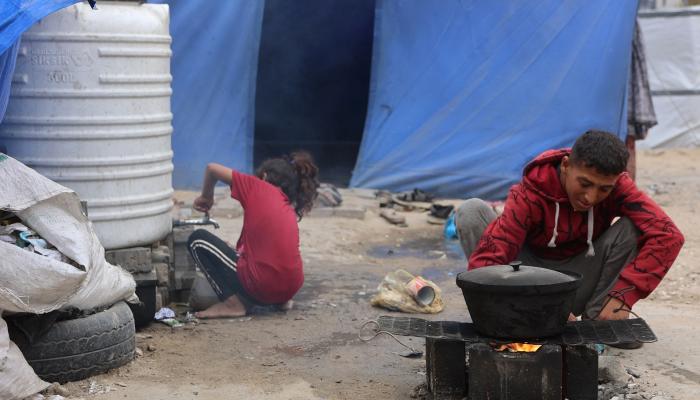 فلسطينيون في مخيم نزوح وسط أنقاض مبنى في مدينة غزة