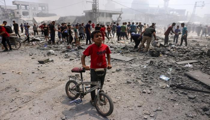 طفل بجانب دراجته، بينما يتفقد فلسطينيون الدمار الذي أعقب غارة إسرائيلية جنوب غزة