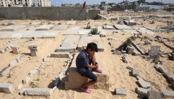 طفل يجلس فوق قبر في خان يونس