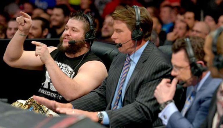 كيفين أوينز يجلس بجانب المذيع قبل أن يفسد النزال الثلاثى