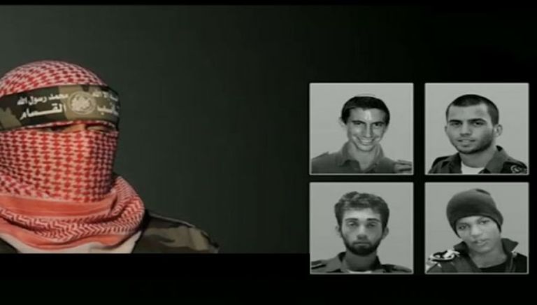 الناطق باسم القسام وخلفه صور الجنود الأربعة