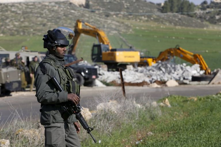 جندي إسرائيلي يقف أمام أحد اللوادر أثناء تنفيذ عملية إزالة لأحد المبان الفلسطينية - رويترز