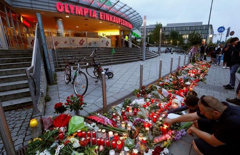أشخاص يضيئون الشموع بجوار أزهار بجانب مركز التسوق الذي وقع بجانبه الحادث - رويتزر