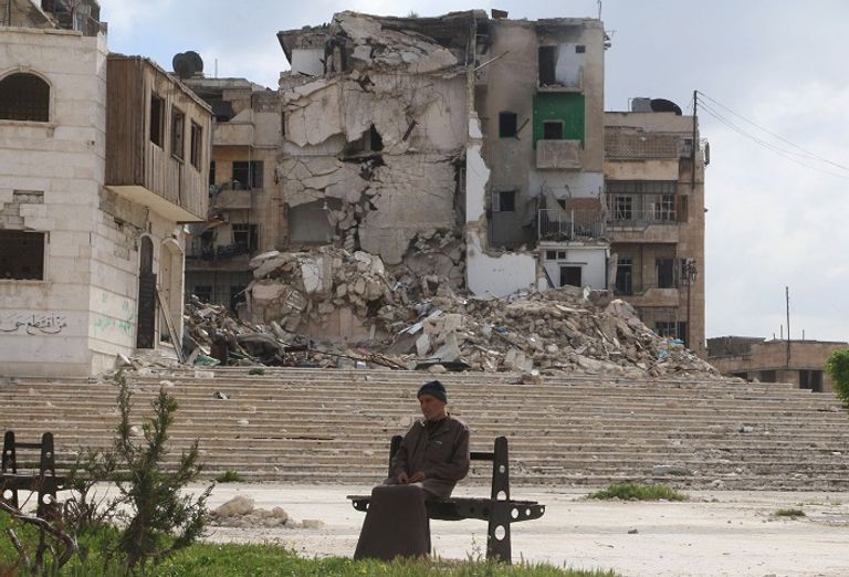 سوري يجلس على مقعد وخلفه مباني مدمرة في حلب (أرشيفية من رويترز)