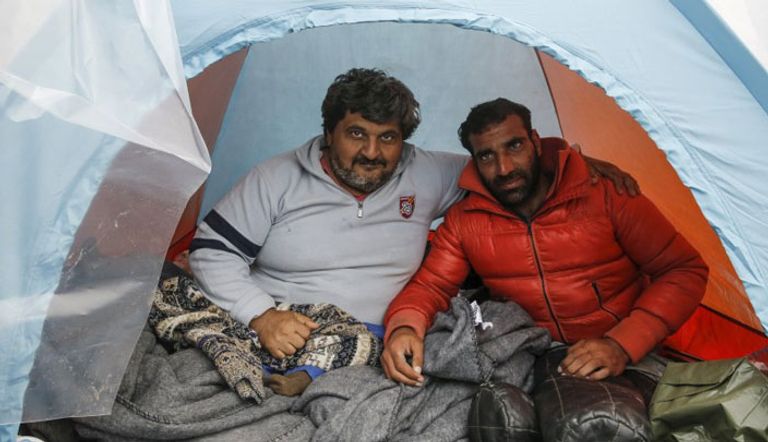 اللاجئ العراقي حسن عمر (إلى اليسار) مع اللاجئ السوري رضوان شيخو داخل خيمة في مخيم مؤقت للاجئين والمهاجرين قرب قرية ايدوميني على حدود اليونان مع مقدونيا (رويترز)
