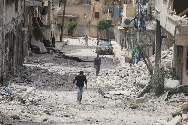 سوريون يسيرون وسط حطام منازل في حلب (رويترز)