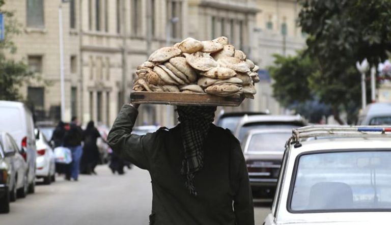 رجل يحمل فوق رأسه خبزًا في شارع بالقاهرة (رويترز)