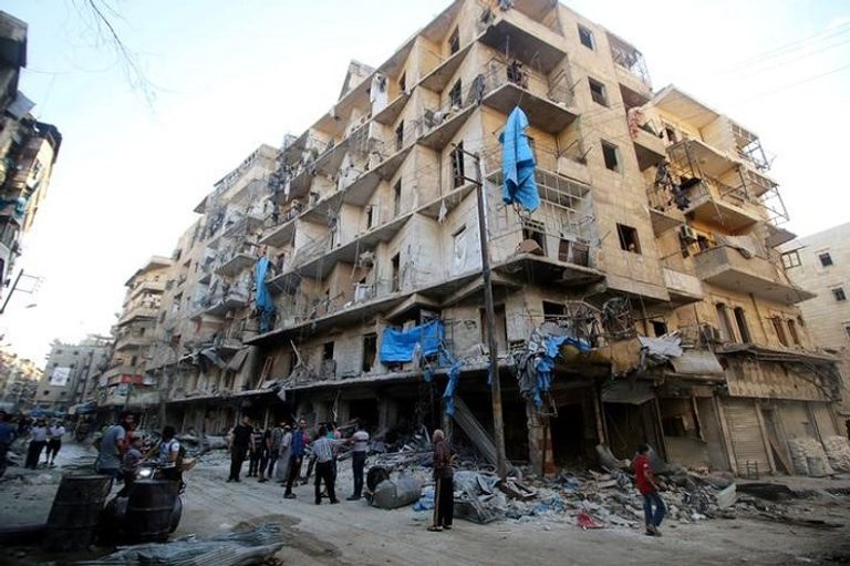 رجال أمام مبنى مدمر في حلب (رويترز)