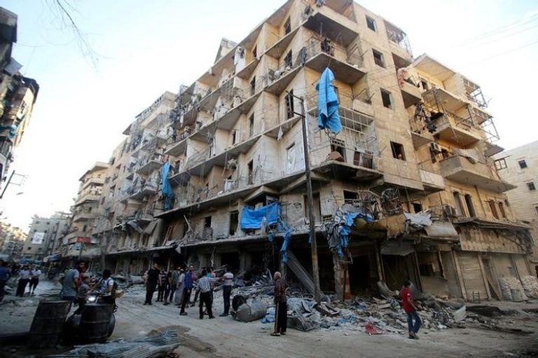 صورة أرشيفية لرجال أمام مبنى مدمر في حلب (رويترز)