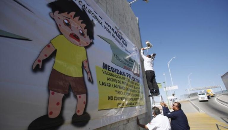 عامل يعلق ملصقا إرشاديا للوقاية من مرض الحصبة في حملة للتوعية في منطقة على الحدود الأمريكية المكسيكية