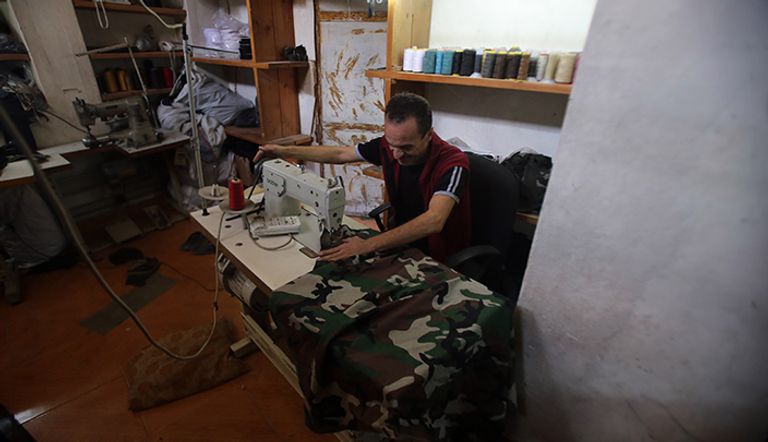 خياط في مدينة حلب القديمة في المناطق التي تسيطر عليها الحكومة يخيط أغطية الرأس العسكري القلعة المدرجة في قائمة اليونسكو  في الجانب الذي تسيطر عليه الحكومة في حلب الشمالية