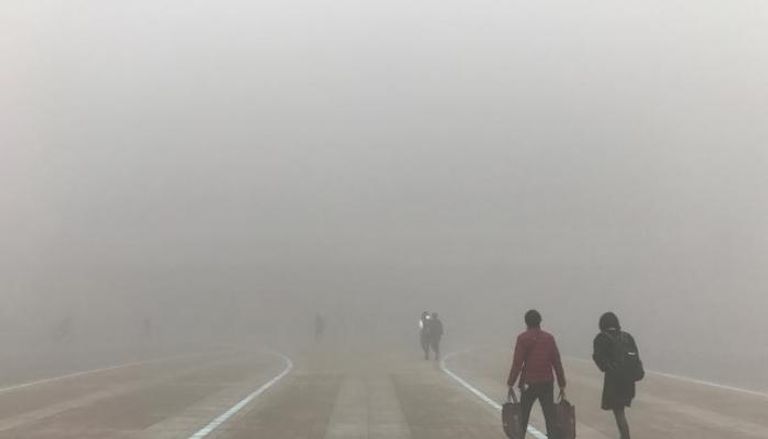 أشخاص يسيرون وسط ضباب دخاني بالصين