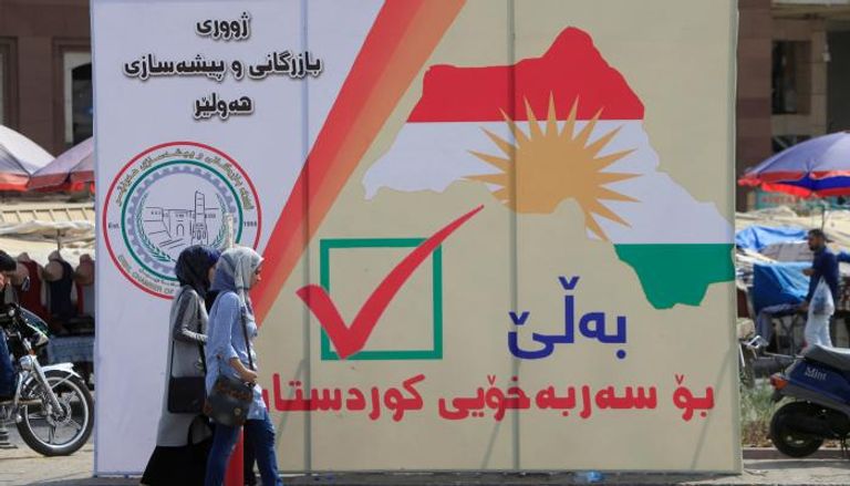 نساء عراقيات يمشين بجانب يافطة كردية للاستقلال بأربيل (رويترز)
