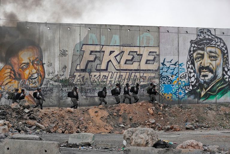 عناصر من جنود الاحتلال يمرون أمام جرافتي فلسطيني على جدار الفصل العنصري