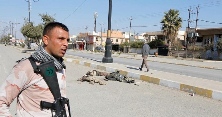 جندي عراقي يقف على مقربة من جثث الدواعش