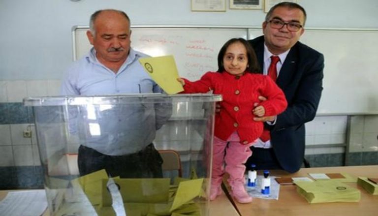 مشرفون يحملون أقصر سيدة بتركيا لوضع ورقتها في صندوق الاقتراع
