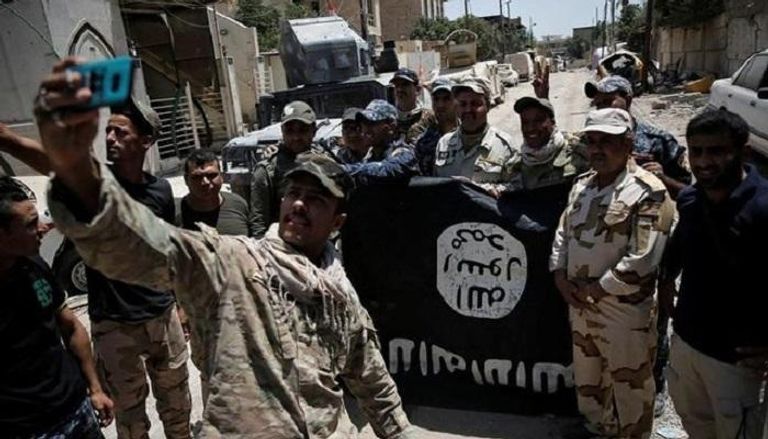 قوات عراقية تلتقط صورا مع علم داعش المقلوب احتفالا بهزيمته (رويترز)