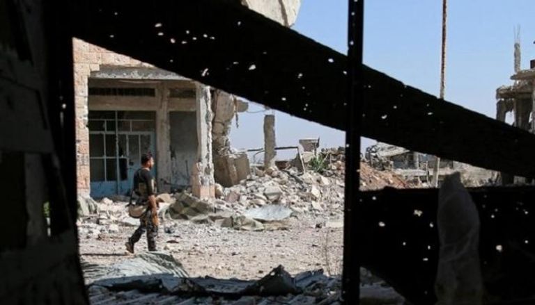 مقاتل سوري من الجيش الحر يسير بين مبانٍ مدمرة في درعا