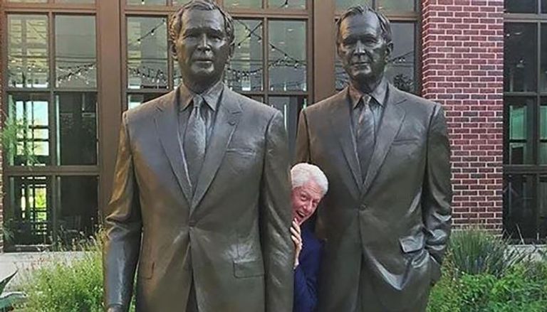 بيل كلينتون وسط تمثالي بوش الأب والابن